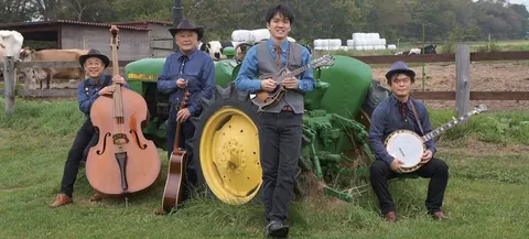 八ヶ岳Mt.Boysの4人。トラクターの前で楽器を持っている